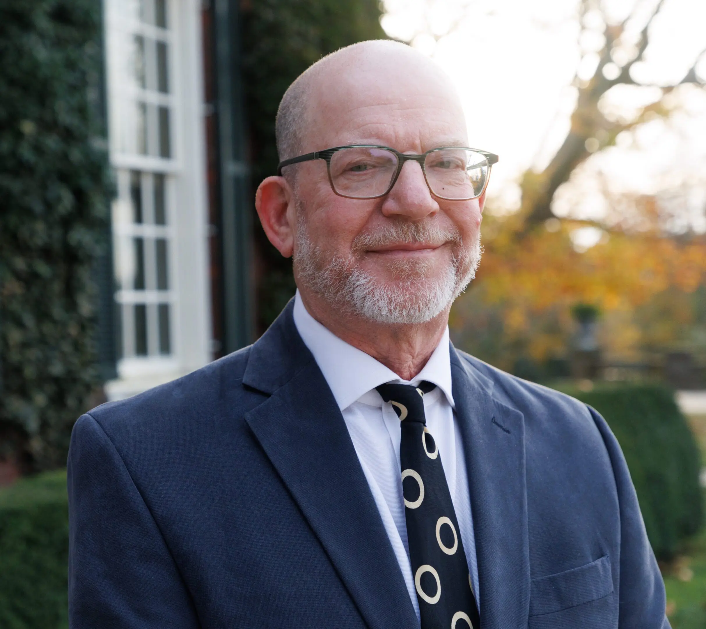 Smiling elderly man in glasses and suit outdoors.