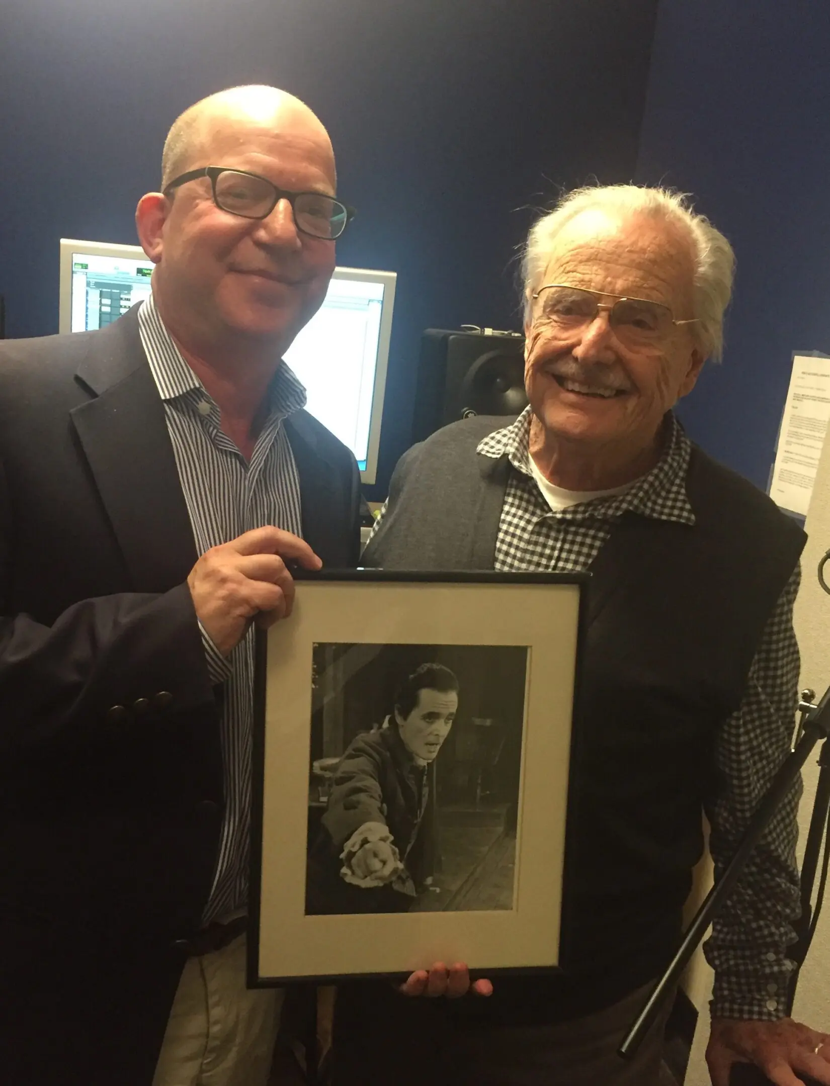 Two men holding a framed black-and-white photo of a young man.